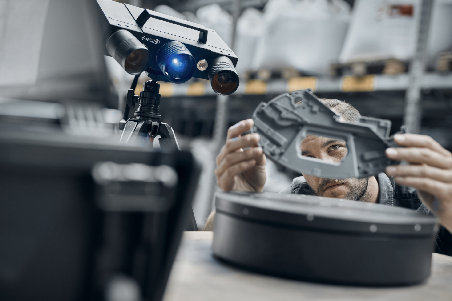 A person inspecting a grey plastic part using a 3D scanner and a rotation table.